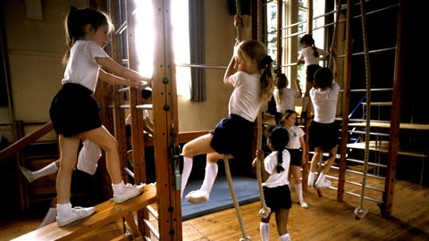 Young children on a climbing frame in a school gymnasium