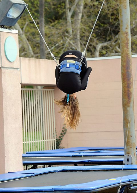 A trampolinist being supported by a harness while performing a somersault