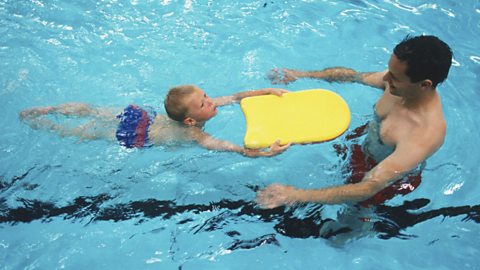 Young boy in swimming pool, using a float to swim towards a man