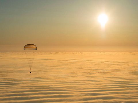 The Soyuz capsule hanging below a parachute returning to Earth.