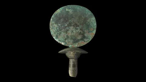 Courtesy Two Temple Place/Macclesfield Museum This copper alloy mirror from the 2nd Millennium BC has a handle made out of stone that looks like a column of papyrus (Credit: Courtesy Two Temple Place/Macclesfield Museum)