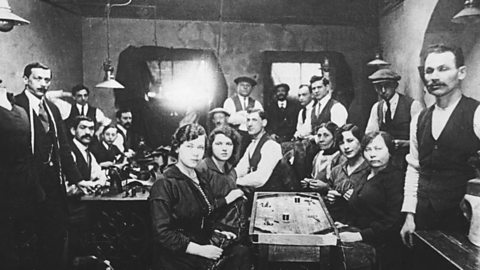 A photograph of thirteen men and five women in a very crowded sweatshop