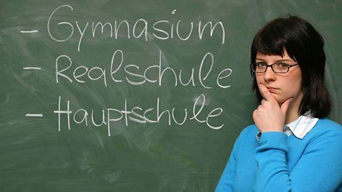 Girl standing infront of chalk board with the words Gymnasium, Hauptschule and Realschule written in chalk