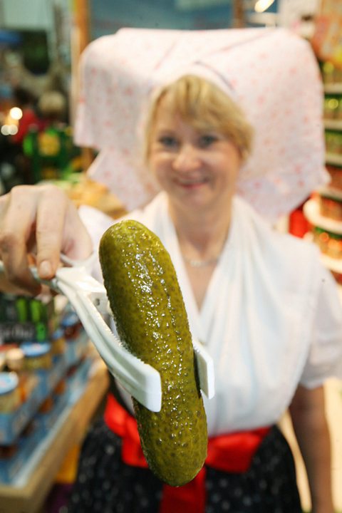 A woman in traditional dress presents a gherkin from the Spreewald region
