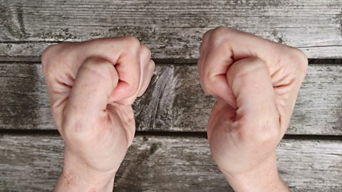 Clenched fists with the thumbs pressing into the fists