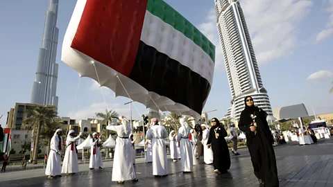 Getty Images Emirati men and women carry a UAE flag in front of the Burj Khalifa during United Arab Emirates National Day, Dubai (Credit: Getty Images)