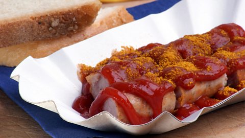 Curried sausage with ketchup on paper plate