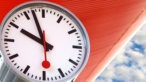 Closeup of a clock against an orange roof and blue sky