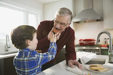 A boy and an older man, preparing food together in a kitchen. 