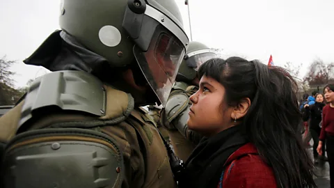 Carlos Vera/Reuters A demonstrator stares at a riot policeman during a protest marking Chile’s 1973 military coup in the capital, Santiago (Credit: Carlos Vera/Reuters)