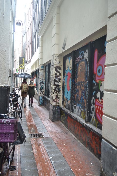 Photograph of people walking down a narrow alley with graffiti on the walls