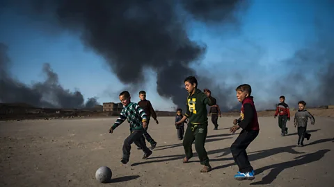 Odd Andersen/AFP/Getty Images Children play football as oil wells, set ablaze by retreating Islamic State fighters, burn behind them in the town of Qayyarah, Iraq (Credit: Odd Andersen/AFP/Getty Images)