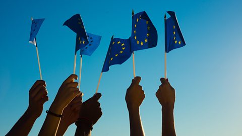 Several people holding European Union flags to the sky with outstretched arms