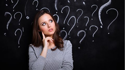 Woman looking thoughtful in front of a blackboard with question marks on it