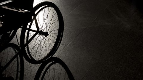 The wheel of a wheelchair on a dark background, its shadow is visible