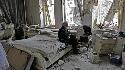 Joseph Eid/AFP Mohammad Mohiedine Anis, 70, smokes a pipe as he sits in his destroyed bedroom listening to music on his record player in Aleppo (Credit: Joseph Eid/AFP)