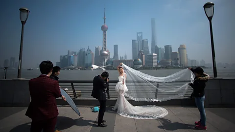 Getty Images A woman poses for a wedding picture at the Bund in front of the financial district of Pudong in Shanghai (Credit: Getty Images)
