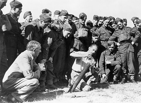 Members of the Home Guard in uniform look on as an instructor demonstrates how to operate a mortar.