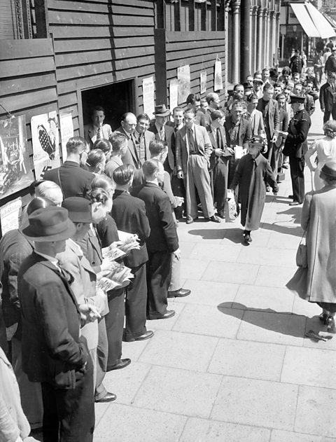 Men in WWII era clothing form a large queue.