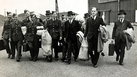 A group of smiling men carrying duffel bags. Some are in uniform, others are in civilian clothing.
