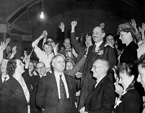 Clement Attlee celebrates surrounded by a cheering crowd.