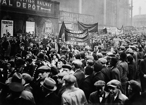 Women marching with a banner that reads 'Women's contingent National Hunger March'. Men and police officers line the streets.
