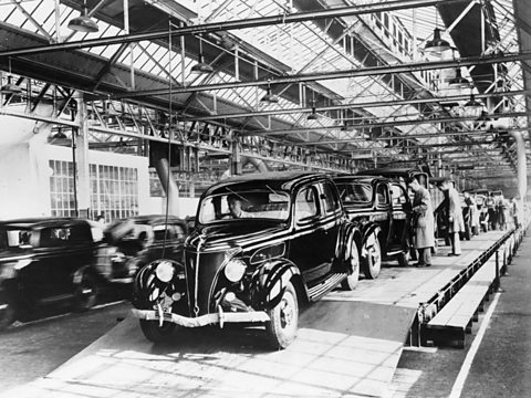 Factory workers work on a production line of identical black Fords