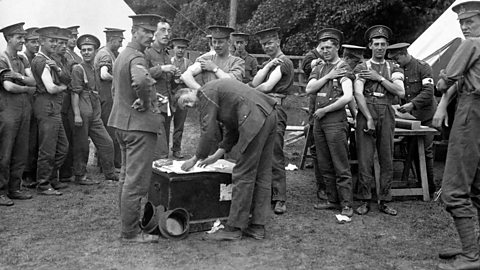 Soldiers in uniform with their sleeves rolled up, waiting in line to receive injections