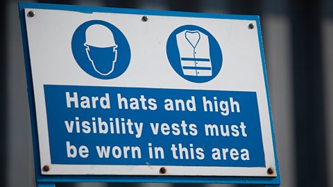 A hard hat and hi-vis jacket safety sign