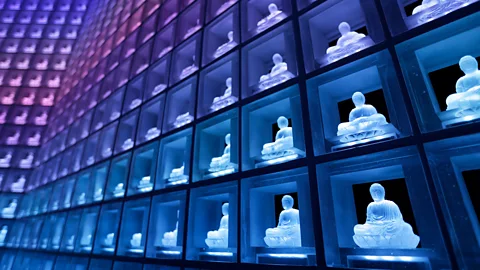 Getty Images In facilities like this one in Japan, ashes are kept in urns behind glowing buddhas - allowing many people to be laid to rest in one room (Credit: Getty Images)