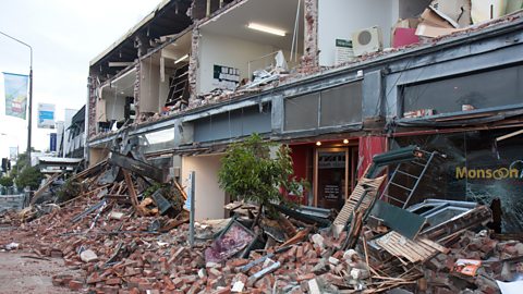 Earthquake-damaged buildings on a street in Christchurch, New Zealand. The fronts of the buildings have been reduced to rubble which now lies in the street.