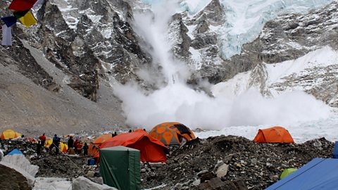 People and tents at Base Camp, Mount Everest. The people are looking at an avalanche which is occurring in the background.