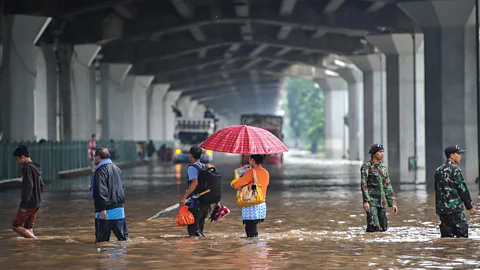 Alamy People stand on a flooded street in Jakarta, which struggles with subsidence (Credit: Alamy)
