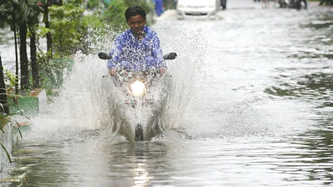 Alamy A man rides his motorcycle along a flooded street in Jakarta, a city facing the twin challenges of sea level rise and subsidence (Credit: Alamy)