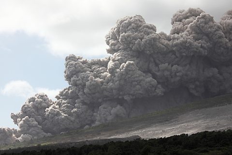 A large cloud of volcanic material flowing down the side of a mountain.