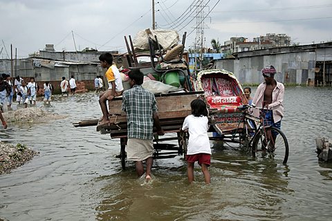 People pushing a wagon piled high with their possessions through a flooded city in Bangladesh.