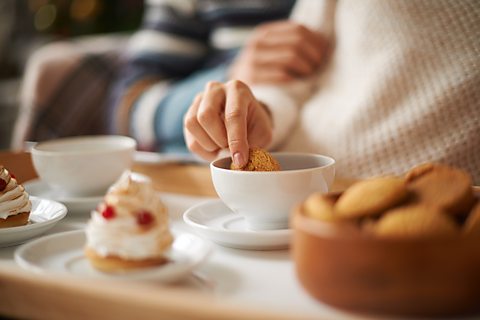 Llun o law hen ddynes yn meddalu bisgedyn mewn cwpanaid o de