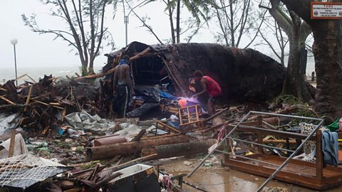 Two people looking through the wreckage of house.