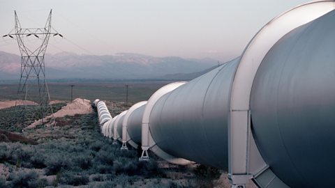 Looking along a large metallic pipeline in the desert.