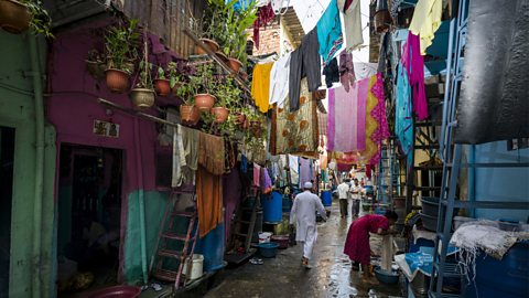 A narrow city street with plant pots hanging from balconies, and washing lines full of colourful clothes hanging across it.