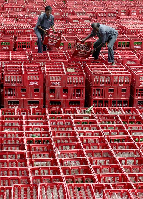 Indian employees at Hindustan Coca-Cola stack a pile of empty bottles in their crates.