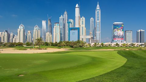 The lush grass of a golf course with a towering skyline in the distance