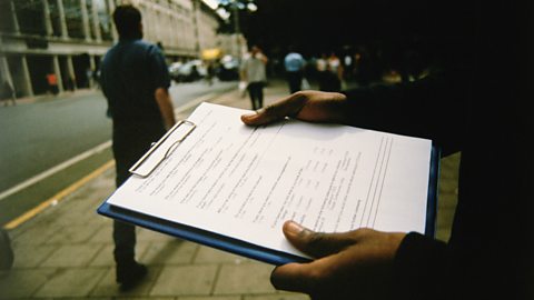 Hands holding a questionnaire on a clipboard in a busy street