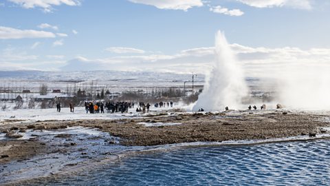 A plume of water bursts into the air with tourists watching.