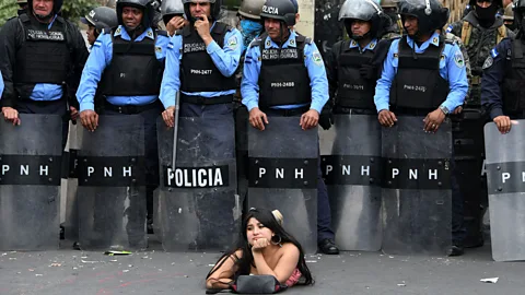 Orlando Sierra/AFP/Getty Images A protestor lies on the street in front of police officers during a demonstration against the contested re-election of President Hernandez in Honduras (Credit: Getty Images)