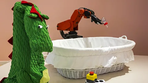 Getty Images A dragon costume is used to make this bottle-feeding industrial robot seem a little more friendly (Credit: Getty Images)