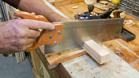 Male hand using tenon saw at woodworking bench