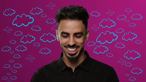 A smiling man looking down and wearing a black shirt. He is standing in front of a pink background with blue clouds on it.