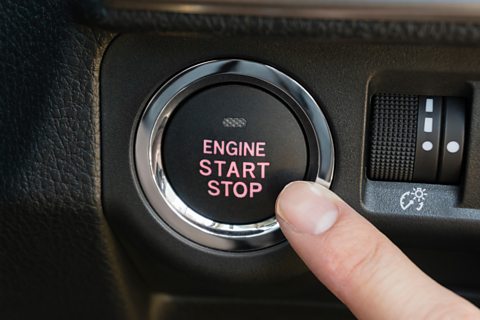 Picture of someone pushing the engine start stop button of a car