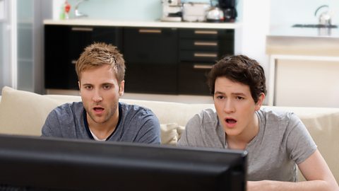 Two teenagers looking surprised at TV screen.